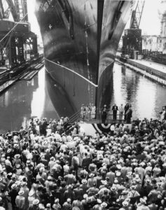 一大群人在停靠在码头上的一艘即将下水的船前。前面是赞助商和嘉宾的平台。